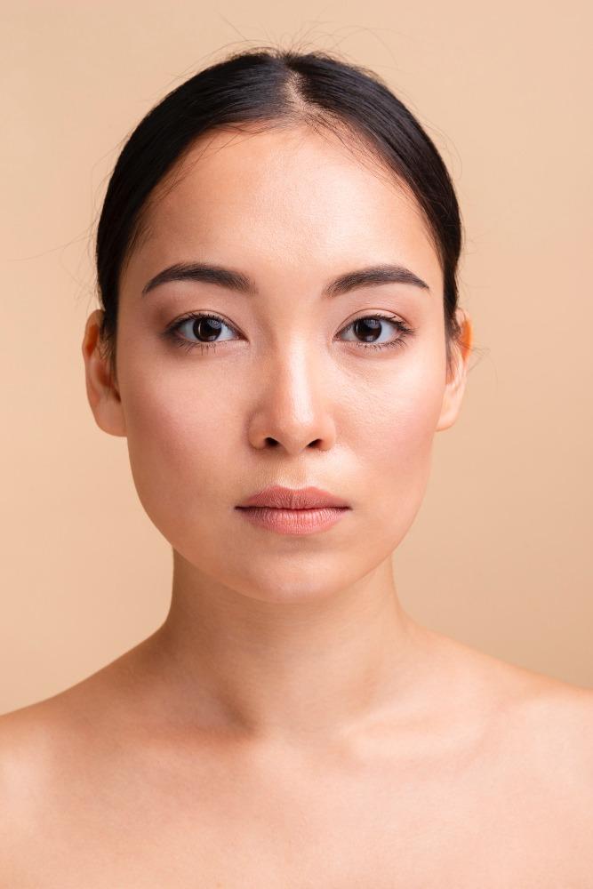 Portrait of a woman with natural makeup and smooth skin, looking directly at the camera against a beige background.