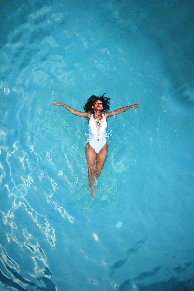 Woman relaxing and floating on her back in a swimming pool, wearing a white swimsuit.