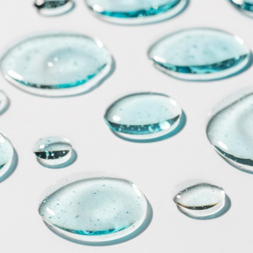 Nahaufnahme von bläulich schimmernden Wassertropfen auf einer weißen Oberfläche.