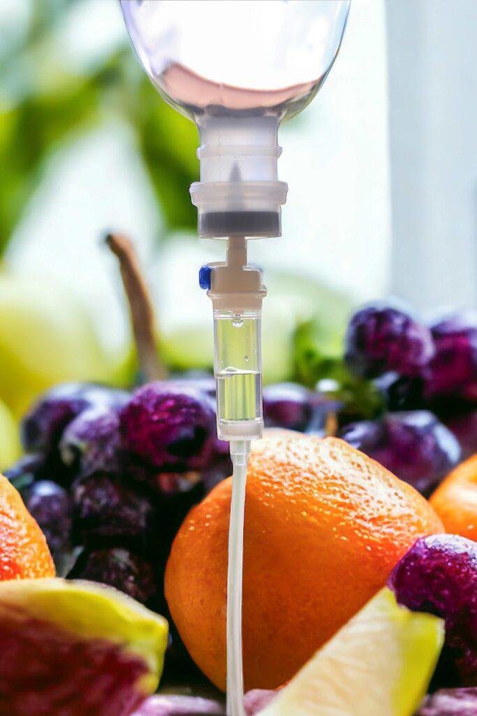 IV-Infusionsset vor Orangen, Trauben und Zitronenscheiben – Symbol für Vitamininfusion.