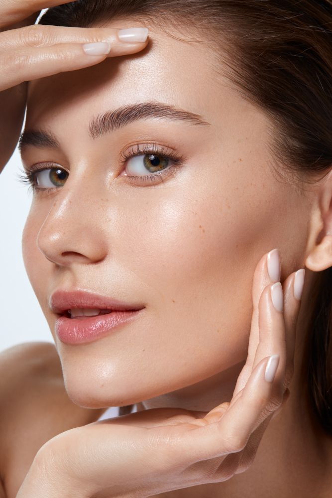 Nahaufnahme einer Frau mit glatter, strahlender Haut; sie rahmt ihr Gesicht mit beiden Händen und blickt leicht seitlich.